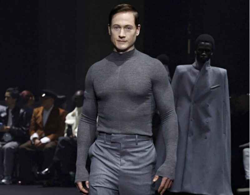 Miliarder teknologi Bryan Johnson mengenakan setelan abu-abu di catwalk Paris Fashion Week.
